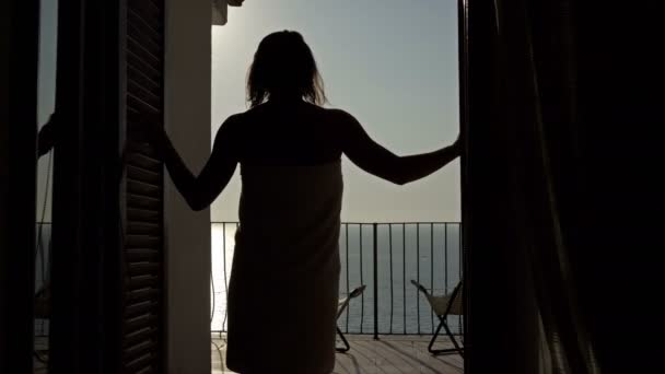 Fille enveloppée dans une serviette, après une douche, sort sur la terrasse pour admirer le coucher de soleil sur la mer. — Video