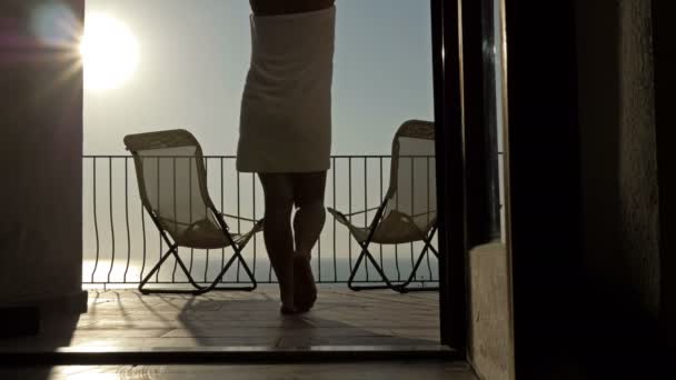 Dziewczyna owinięta w ręcznik, po prysznicu, wychodzi na taras podziwiać zachód słońca nad morzem. — Wideo stockowe