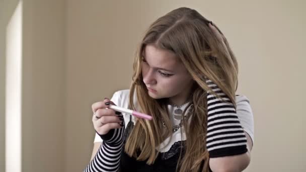 Tonårstjej ser skräckinjagande på ett graviditetstest. — Stockvideo
