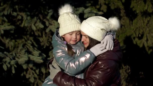 一个7-8岁的年轻女子和一个7-8岁的女孩温柔地相互拥抱。妈妈和女儿在冬天的森林里散步。家庭假. — 图库视频影像