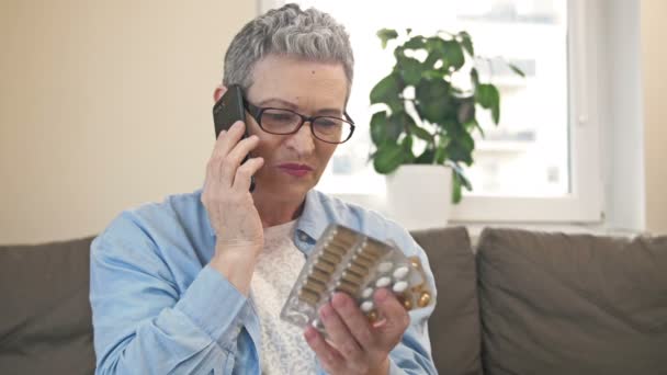 Donna matura consulta qualcuno al telefono prima di prendere la medicina di cui ha bisogno. — Video Stock