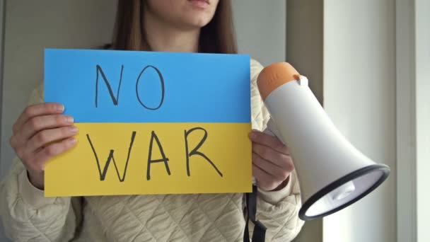 Молода жінка з плакатом і мегафоном у руках вимагає припинення війни в Україні.. — стокове відео