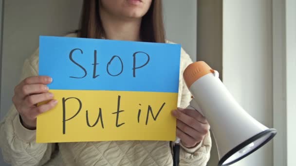 Молода жінка з плакатом STOP PUTIN і мегафон в її руках закликають до припинення війни в Україні.. — стокове відео