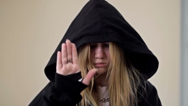 Девушка-подросток, прикрывающая лицо капюшоном, демонстрирует жест, указывающий на то, что человеку нужна помощь.. — стоковое видео