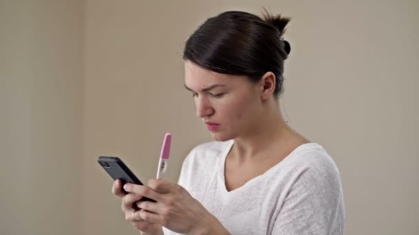 Young woman is happy to see a positive pregnancy test. She hurries to share her joy on the phone with a loved one. — Stock Video