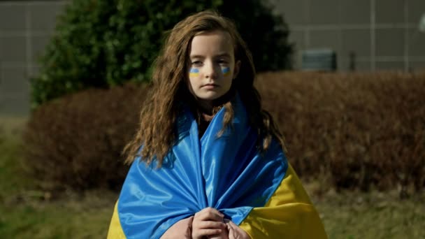Triest meisje van 9-10 jaar met de Oekraïense vlag op haar schouders. Oorlog in Oekraïne. Kinderen van Oekraïne. — Stockvideo