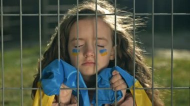 Küçük kız Ukrayna bayrağıyla kaplı ve gözleri metal bir ızgaranın arkasında kapalı. Özgürlüğün eksikliğinin sembolü. Ukrayna 'da Savaş.