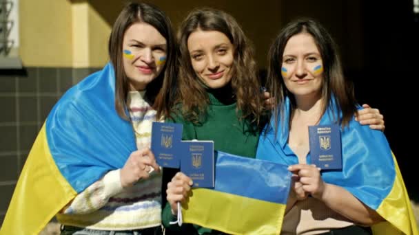 Tres mujeres cubiertas con la bandera de Ucrania se destacan abrazando. En manos de pasaportes ucranianos. Detener la agresión rusa en Ucrania. — Vídeos de Stock