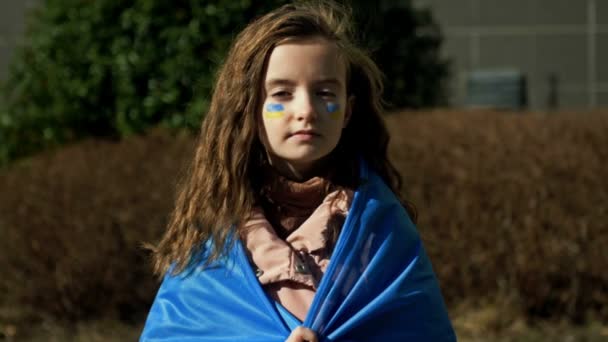 Cara séria de uma menina. As bochechas das crianças são pintadas com as cores amarela e azul da bandeira ucraniana. Crianças pedem paz. — Vídeo de Stock