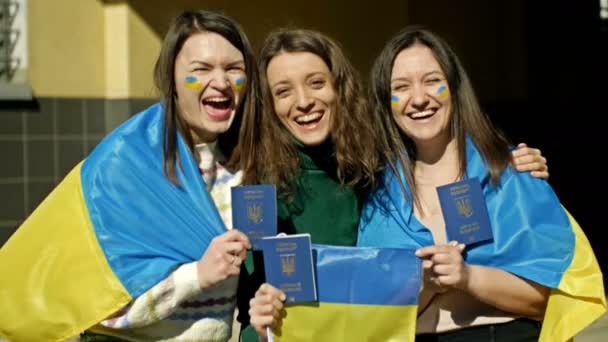 Tres mujeres cubiertas con la bandera de Ucrania se destacan abrazando. En manos de pasaportes ucranianos. Detener la agresión rusa en Ucrania. — Vídeos de Stock