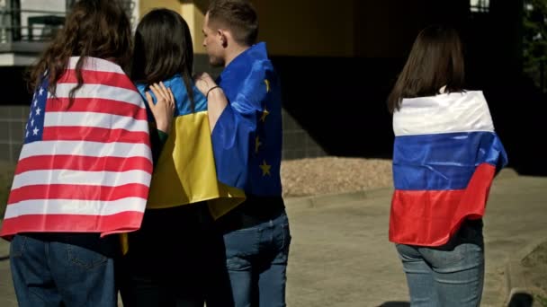 Gruppo di abbracciare le persone con le bandiere di Ucraina, Stati Uniti e Unione europea. Simbolo di solidarietà e sostegno. Una donna con una bandiera russa è sola. — Video Stock