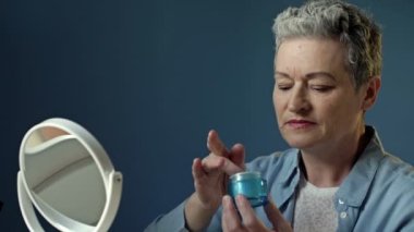 Yaşlı bir kadın yaşlanma önleyici nemlendirici uygular. Emekliler onun görünüşüyle ilgileniyor, kozmetik işlemler yapıyor. Cilt tazeleme, yenilenme ve kaldırma için krem kullanıyor..