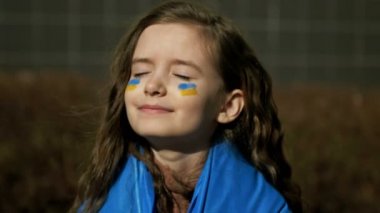 9-10 yaşlarında, omuzlarında Ukrayna bayrağı olan bir kız. Ukrayna 'da savaş. Ukrayna 'nın Çocukları.