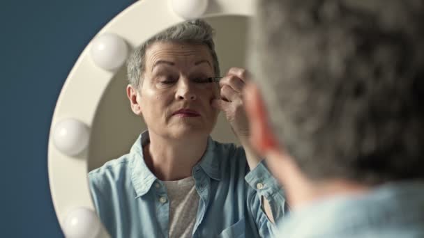 Senior kvinna gör smink framför spegeln. — Stockvideo