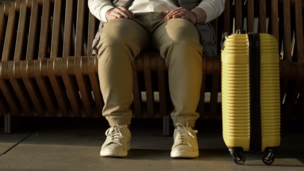 Pernas de um homem sentado num banco à espera do seu voo. Ao lado dele está uma mala amarela.. — Vídeo de Stock
