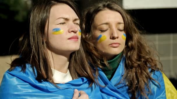 Mujeres con la bandera de Ucrania sobre sus hombros, mirando a la distancia con emoción y esperanza. Protesta contra la guerra en Ucrania y la agresión rusa. — Vídeos de Stock