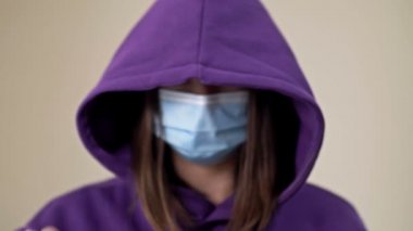 Kapüşonlu ve tıbbi maskeli bir kadın yardıma ihtiyacı olduğunu gösteren bir jest sergiliyor. Covid-19 'da aile içi şiddet vakaları.