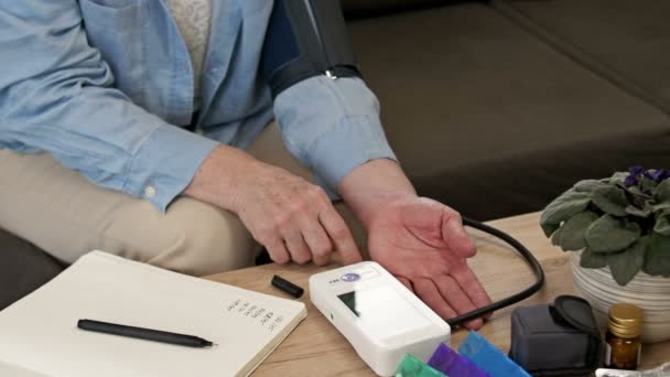 Eine ältere Frau misst ihren Blutdruck und schreibt die Ergebnisse in ein Notizbuch. Heimatüberwachung. — Stockvideo