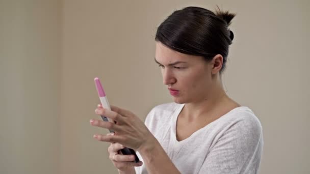 Молодая женщина рада видеть положительный тест на беременность. Она спешит поделиться своей радостью по телефону с любимым человеком. — стоковое видео