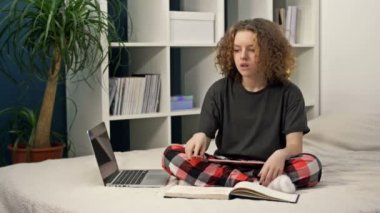 Mesafe öğrenme zorluğu. Genç kız ödevini yapıyor. Evdeki yatakta oturuyor. Her şey yolunda değil, kız üzgün..