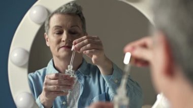 Güzel yaşlı kadın cilt bakımı için nemlendirici ve besleyici bir kozmetik ürün uyguluyor..