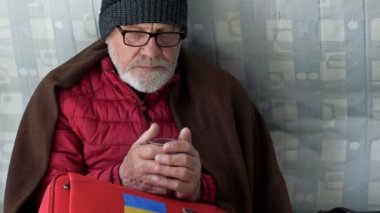 Çay içen üzgün, yaşlı bir Ukraynalı mültecinin portresi. Yerleştirme merkezinin zemininde oturuyor..