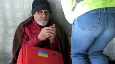 Gönüllü kız, yaşlı bir Ukraynalı mülteciye sıcak çay ikram ediyor, göçmenler merkezinde oturuyor. Ukrayna 'da Savaş.