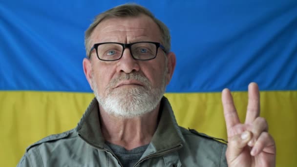 Anciano hombre de pelo gris en el fondo de la bandera de Ucrania. Gesto del ganador. — Vídeos de Stock