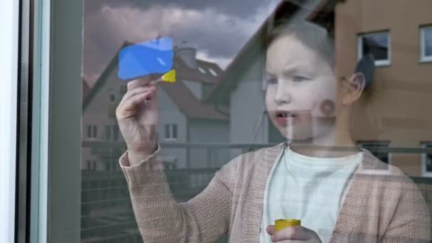 Pencereye Ukrayna bayrağını çizen küçük kız. — Stok video
