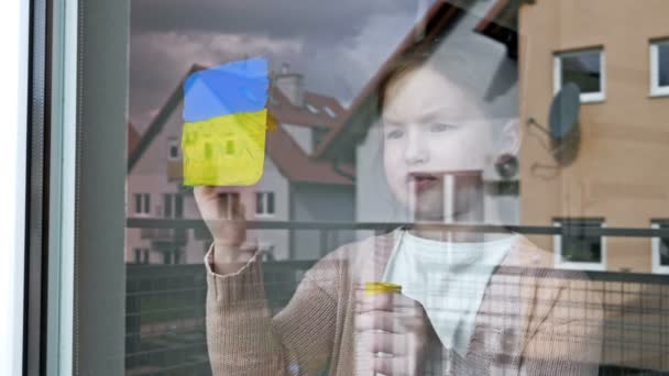 Kleines Mädchen malt die Fahne der Ukraine ans Fenster. — Stockvideo