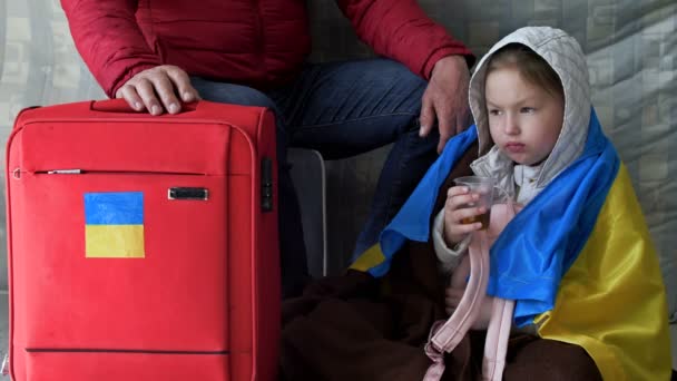 Réfugiés d'Ukraine. Un homme âgé et sa petite-fille attendent de l'aide dans un centre de réinstallation. L'enfant a un drapeau de l'Ukraine sur ses épaules. Guerre de Russie contre l'Ukraine. — Video