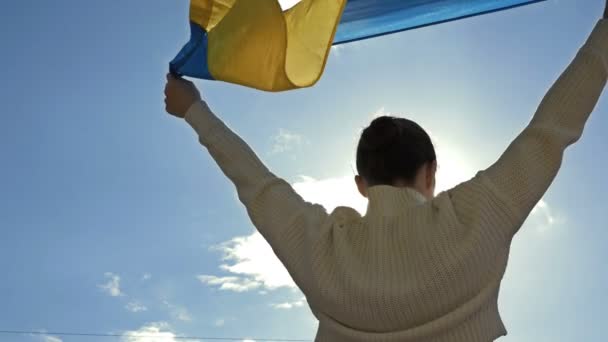 Жінка тримає махаючий прапор України проти блакитного неба.. — стокове відео