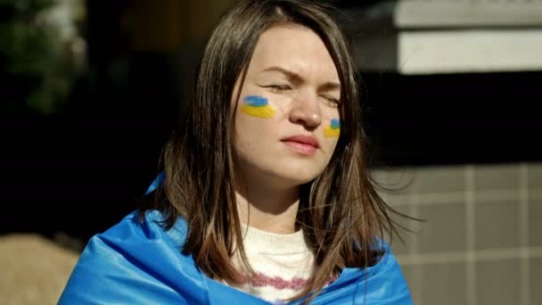 Retrato de una mujer con una bandera ucraniana sobre sus hombros. Protesta contra la guerra en Ucrania y la agresión rusa. — Vídeos de Stock