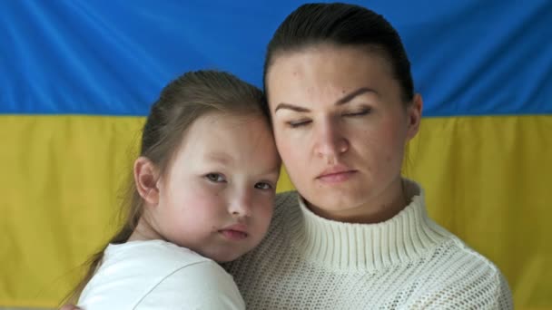 Ung kvinna med sin dotter på bakgrunden av flaggan i Ukraina. Rysslands aggressiva krig mot Ukraina. — Stockvideo