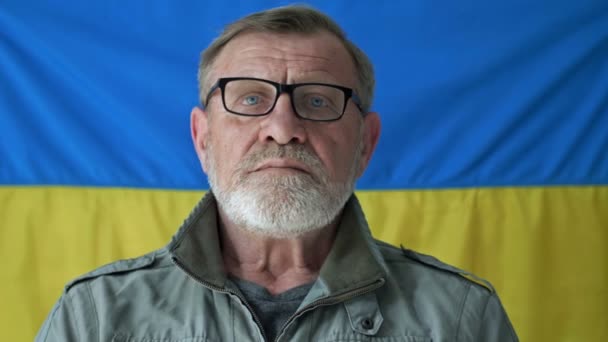Uomo anziano dai capelli grigi sullo sfondo della bandiera dell'Ucraina. — Video Stock
