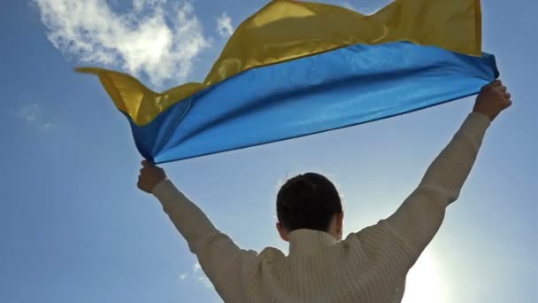 Жінка тримає махаючий прапор України проти блакитного неба.. — стокове відео