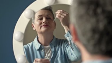 Güzel yaşlı kadın cilt bakımı için nemlendirici ve besleyici bir kozmetik ürün uyguluyor..