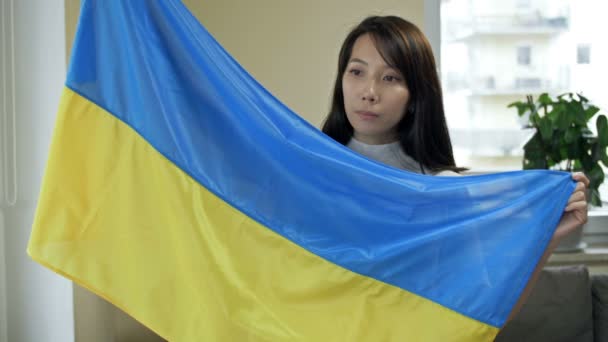 उसके हाथों में यूक्रेनी ध्वज के साथ एक एशियाई महिला का चित्र। यूक्रेन और रूसी आक्रामकता में युद्ध के खिलाफ विरोध . — स्टॉक वीडियो