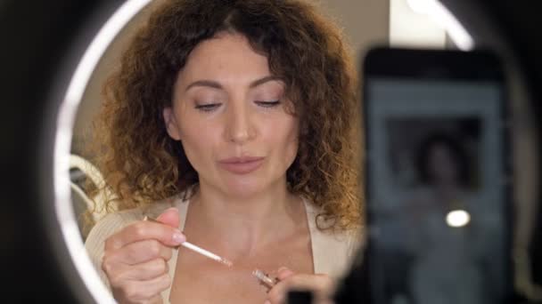 Handsome middelbare leeftijd schoonheid blogger praat over lippenstift en brengt lippenstift op haar hand, pronken met de kleur. Vrouw zit voor een spiegel. — Stockvideo