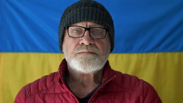Älterer grauhaariger Mann vor dem Hintergrund der Flagge der Ukraine. — Stockvideo