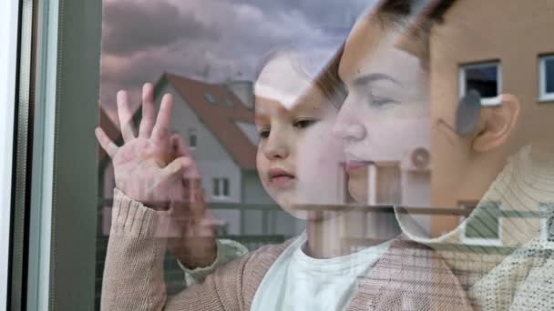 Madre e figlioletta stanno abbracciati e guardano tristemente fuori dalla finestra. — Video Stock