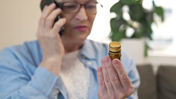 Dojrzała kobieta konsultuje się z lekarzem przez telefon przed zastosowaniem leku, którego potrzebuje. — Wideo stockowe