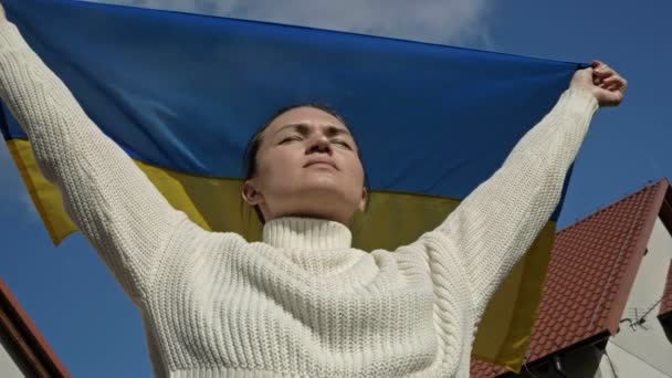 Vrouw houdt een wapperende vlag van Oekraïne tegen een blauwe lucht. — Stockvideo