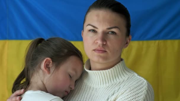 Jonge vrouw met haar dochter op de achtergrond van de vlag van Oekraïne. De agressieve oorlog van Rusland tegen Oekraïne. — Stockvideo