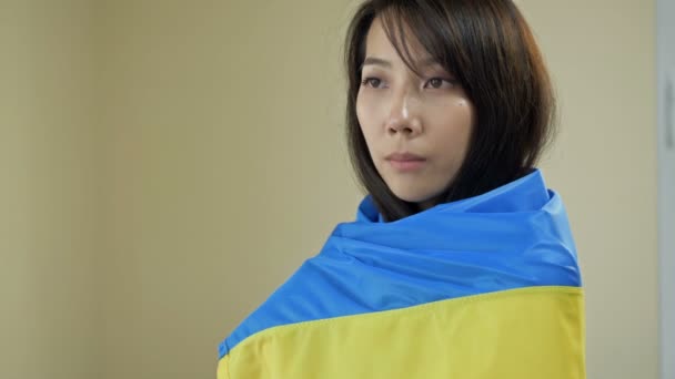 Portrait of an Asian woman with a Ukrainian flag on her shoulders. Protest against the war in Ukraine and Russian aggression. — стоковое видео