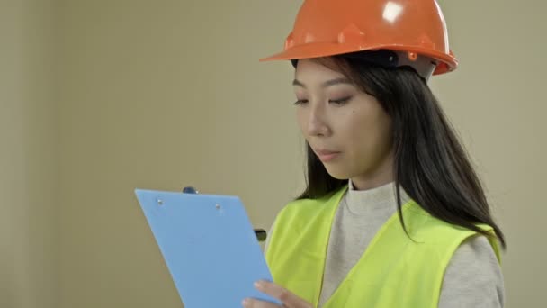 Asian builder woman, wearing protective clothing and a helmet, is writing down something. — Stock Video