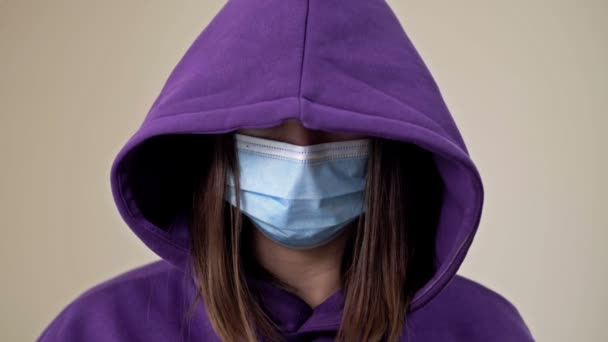 Женщина в капюшоне и медицинской маске демонстрирует жест, указывающий на необходимость помощи. Случаи домашнего насилия во время самоизоляции Covid-19. — стоковое видео