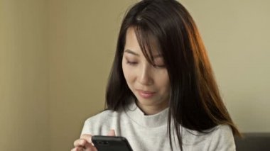 Portrait of a young Asian woman with a mobile phone in her hands.