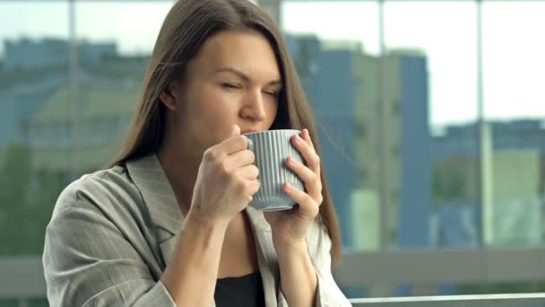 Beautiful young businesswoman drinking hot tea or coffee while standing on the office balcony. — Stockvideo