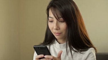 Portrait of a young Asian woman with a mobile phone in her hands.